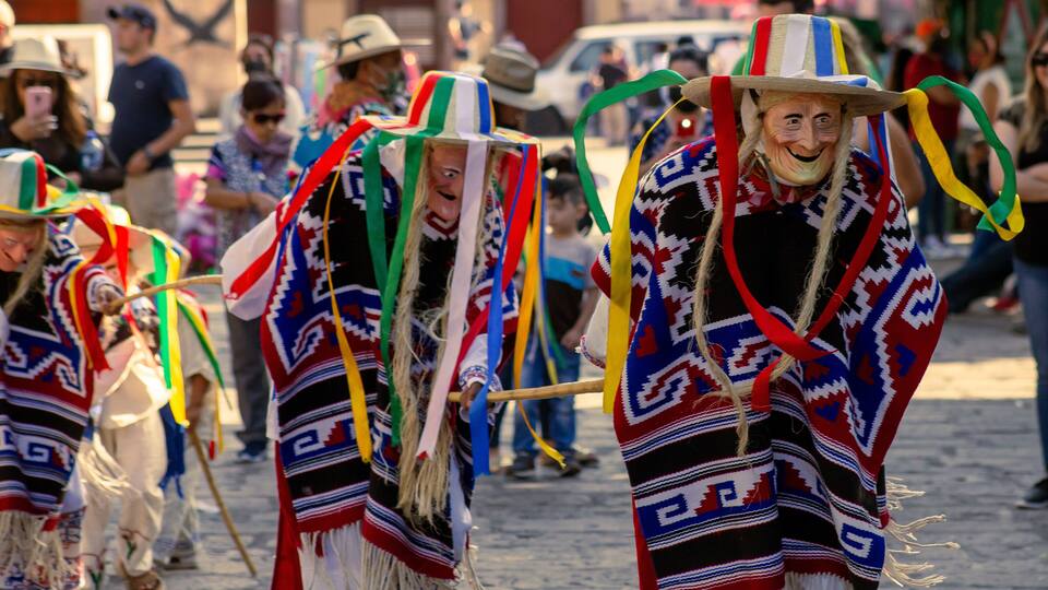 A group of people in traditional attire with colorful patterns and hats, walking on a cobblestone street.