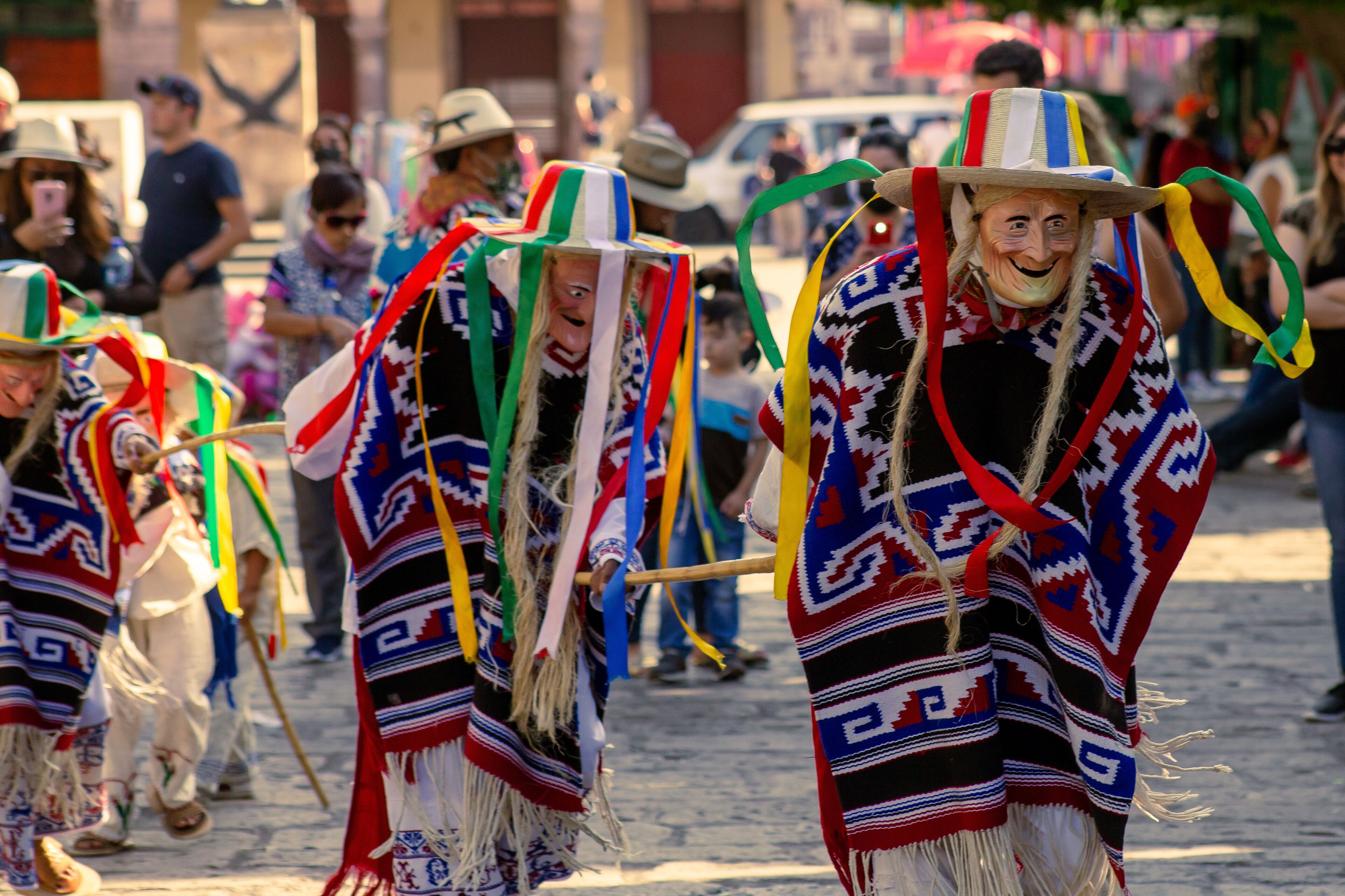 A group of people in traditional attire with colorful patterns and hats, walking on a cobblestone street.