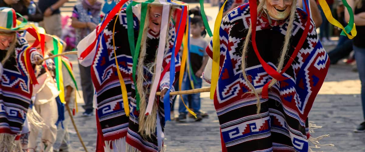 A group of people in traditional attire with colorful patterns and hats, walking on a cobblestone street.