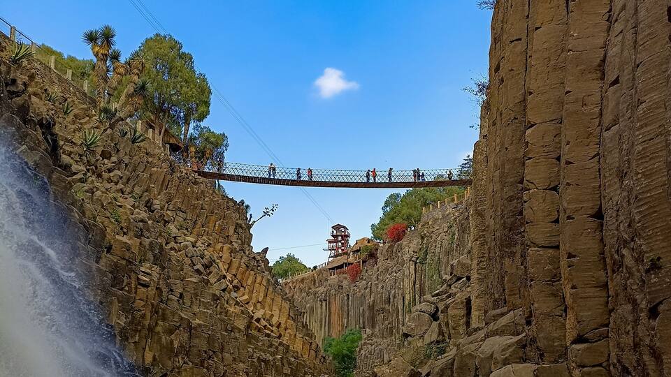 A river flowing through a canyon with a suspension bridge and a waterfall.