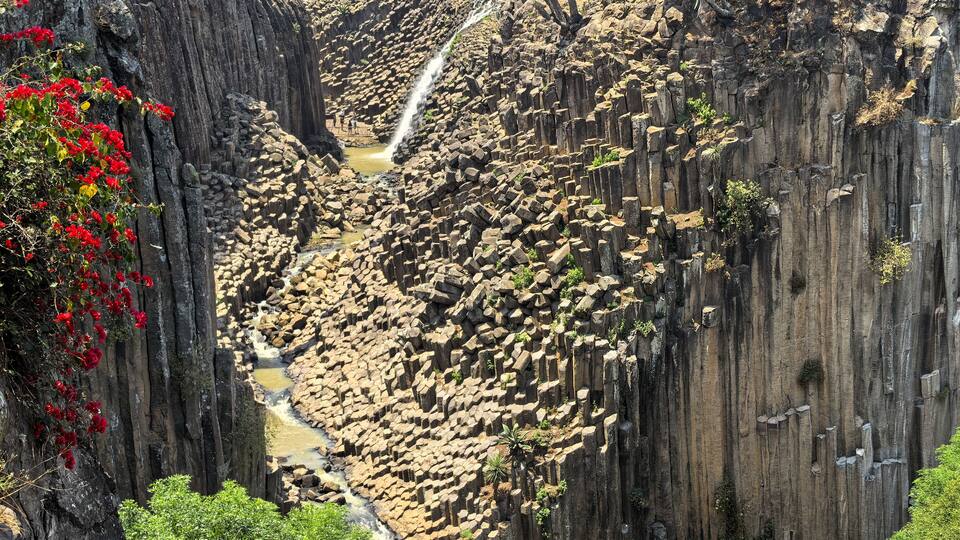 A waterfall cascading down a rocky gorge with a wooden bridge overhead.
