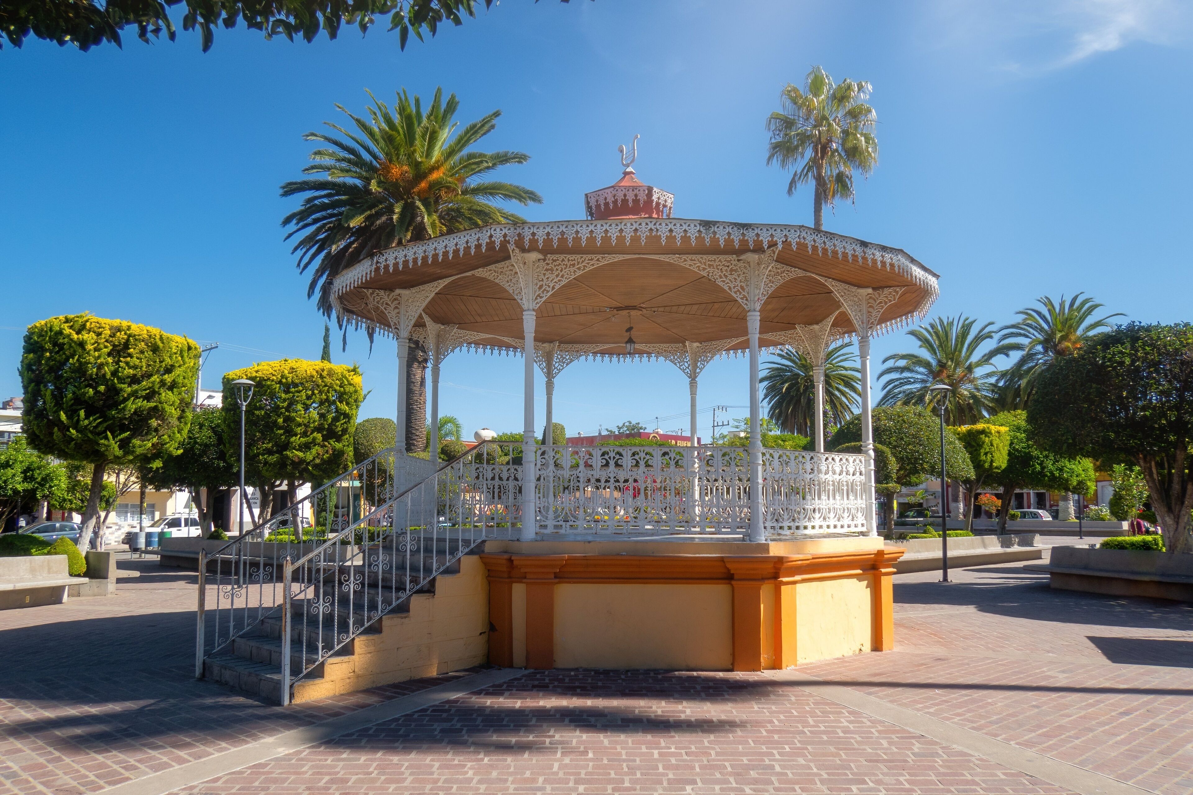 A white gazebo with intricate designs, surrounded by palm trees and a brick pathway.