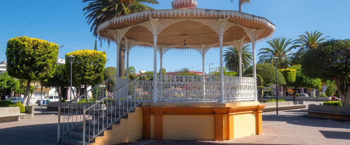 A white gazebo with intricate designs, surrounded by palm trees and a brick pathway.