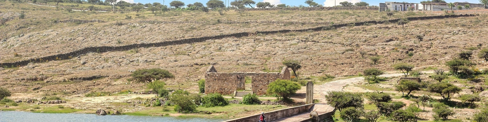 Una gran presa con una persona en bicicleta, un río y un paisaje montañoso con vegetación escasa.