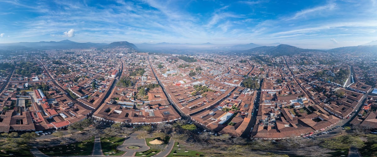 An aerial view of a city with a central grid of streets, surrounded by mountains.