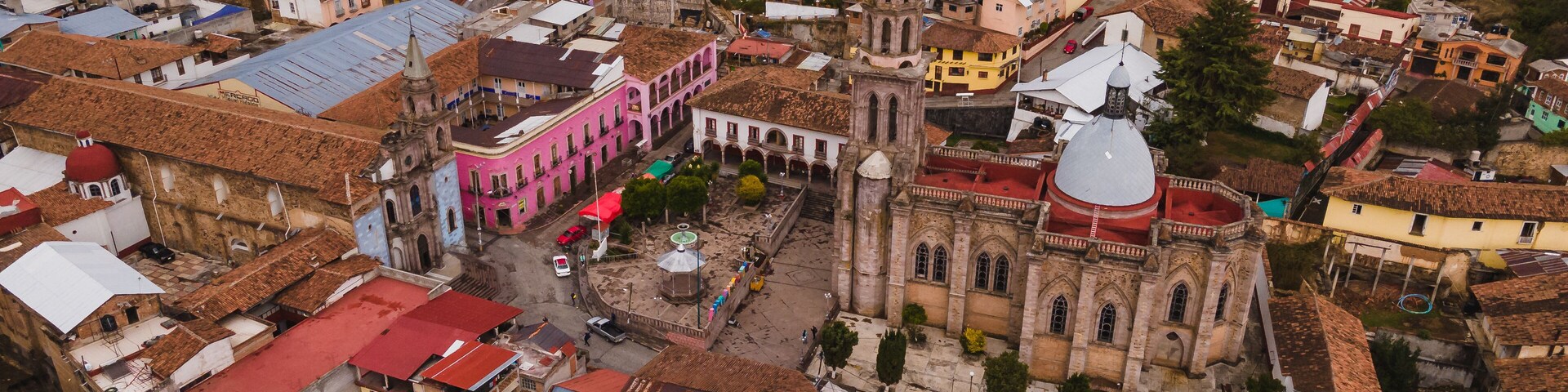 An aerial view of a historic town with colorful buildings, a prominent church with a dome, and a central plaza.