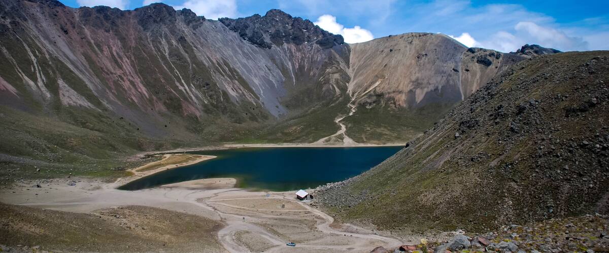 A mountainous landscape with a lake, a dirt road, and a small building.