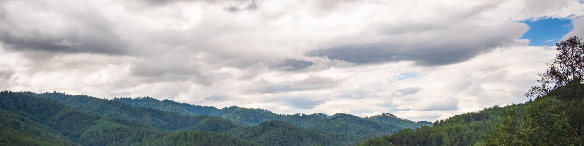 A town nestled in a valley surrounded by lush green hills and a cloudy sky.