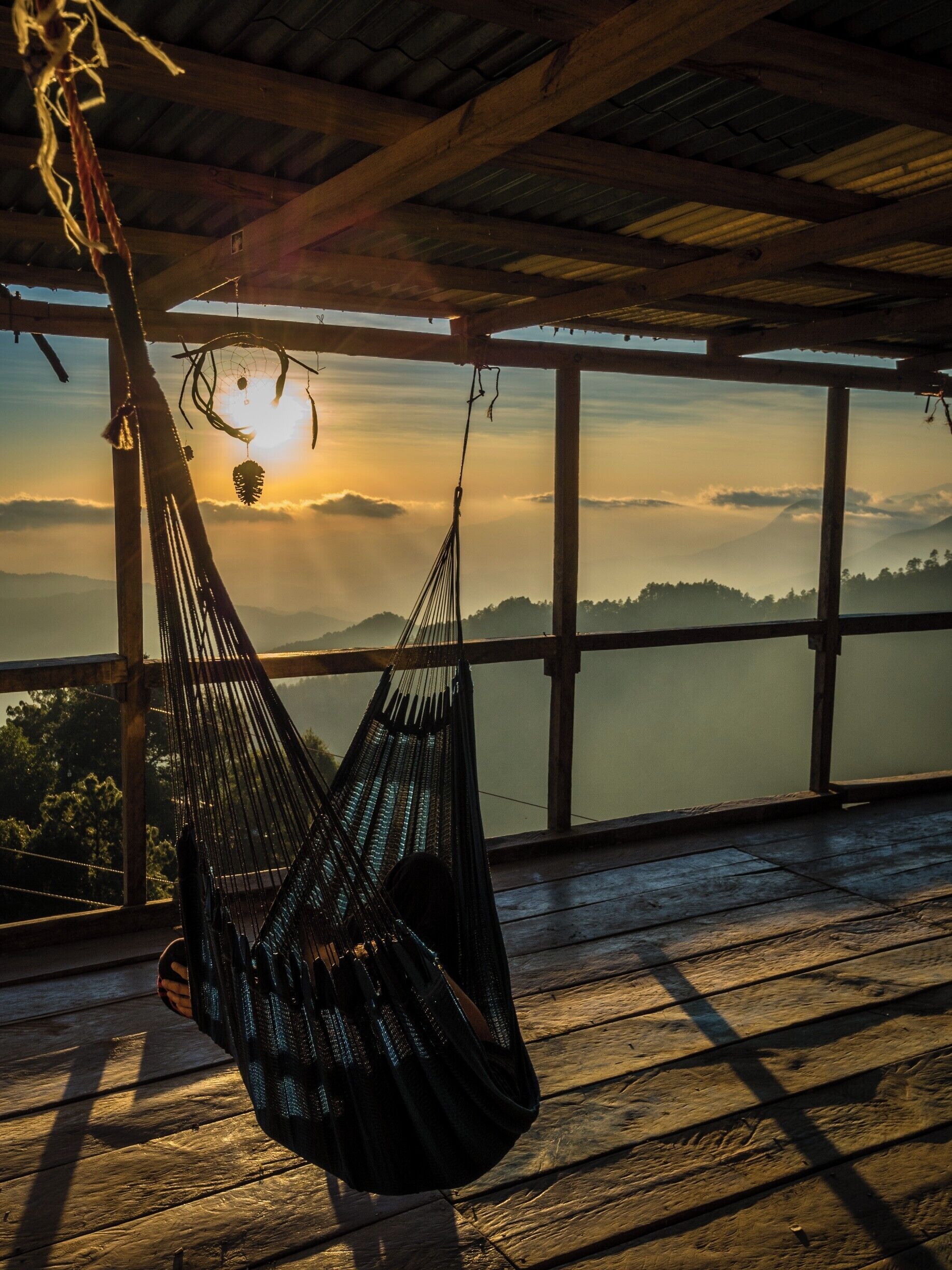 A hammock hanging indoors with a view of a sunset over a mountainous landscape.