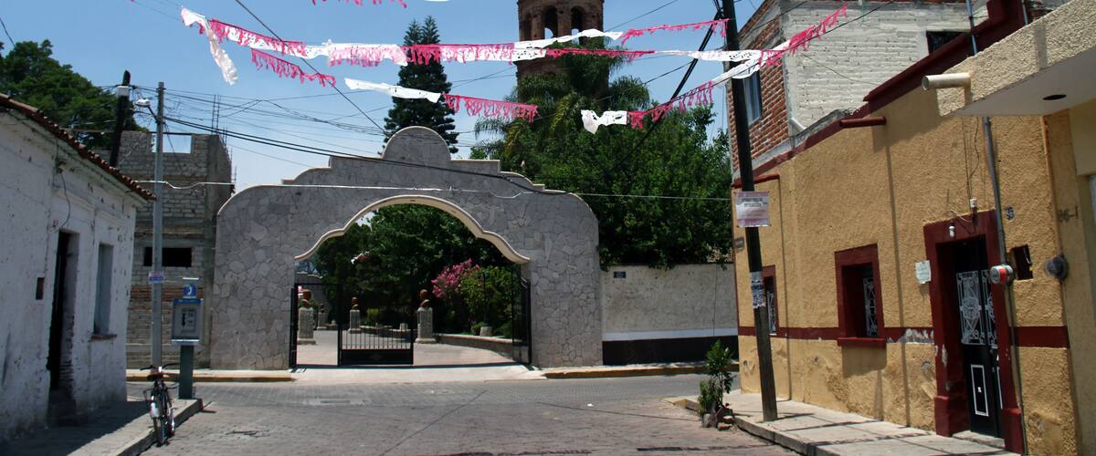 A street with a stone archway, a bell tower, and pink and white banners.