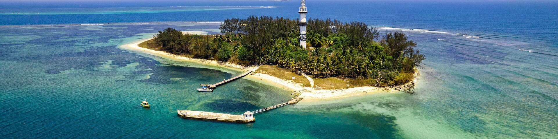 An island with a lighthouse, clear turquoise waters, and a small pier.