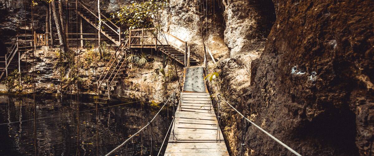A wooden suspension bridge over a river in a rocky gorge.
