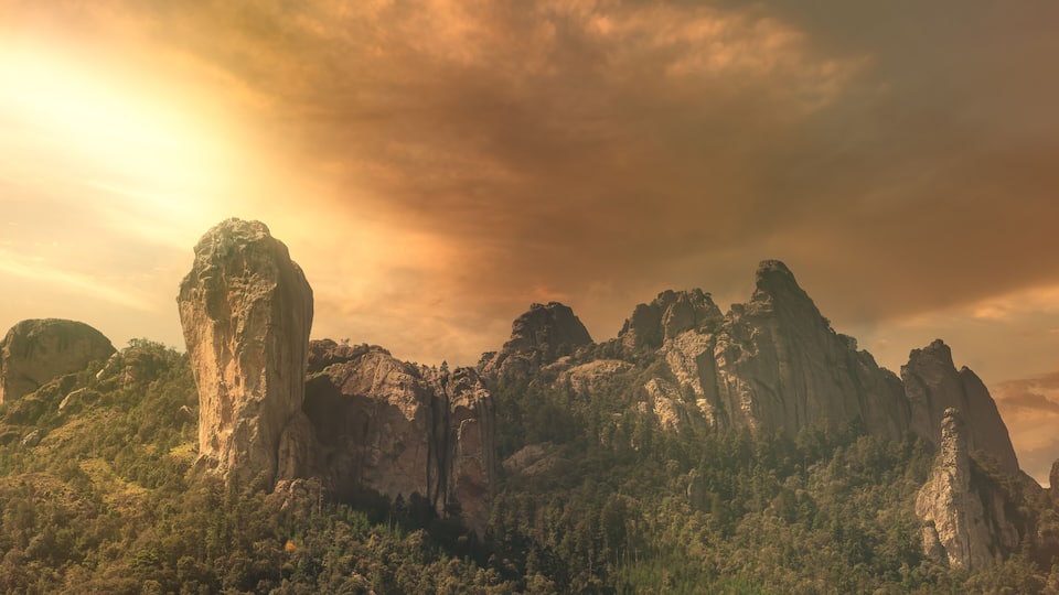 A mountainous landscape with prominent rock formations and dense forest.