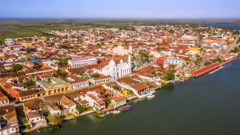 A coastal town with colorful buildings, a prominent white church, and a waterfront with boats.