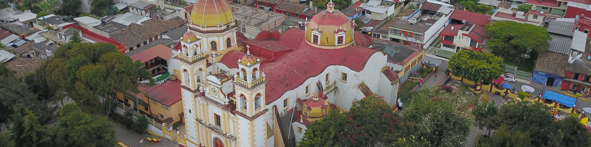 Vista aérea de uma cidade com uma igreja imponente, destacando-se por uma cúpula grande e duas menores, cercada por edifícios residenciais e vegetação.