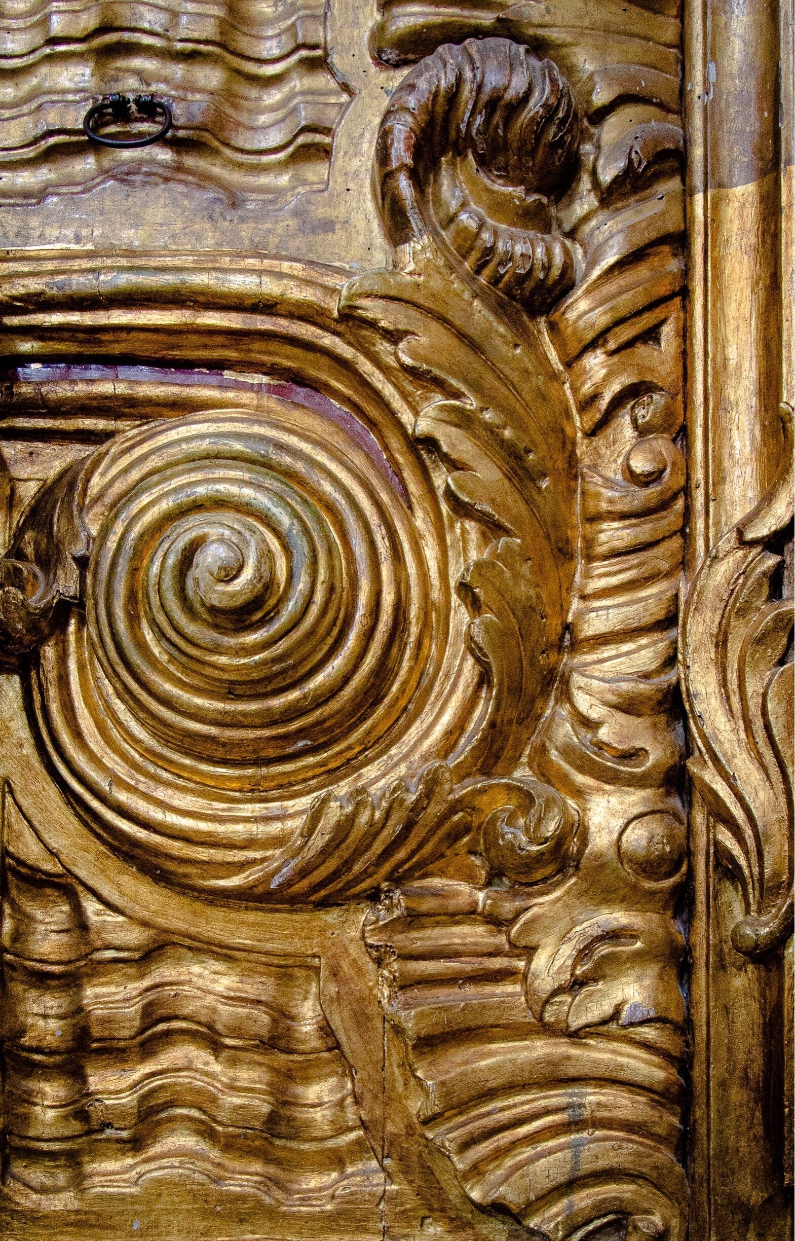 A detailed golden relief sculpture with a central spiral design and ornate leaf patterns.