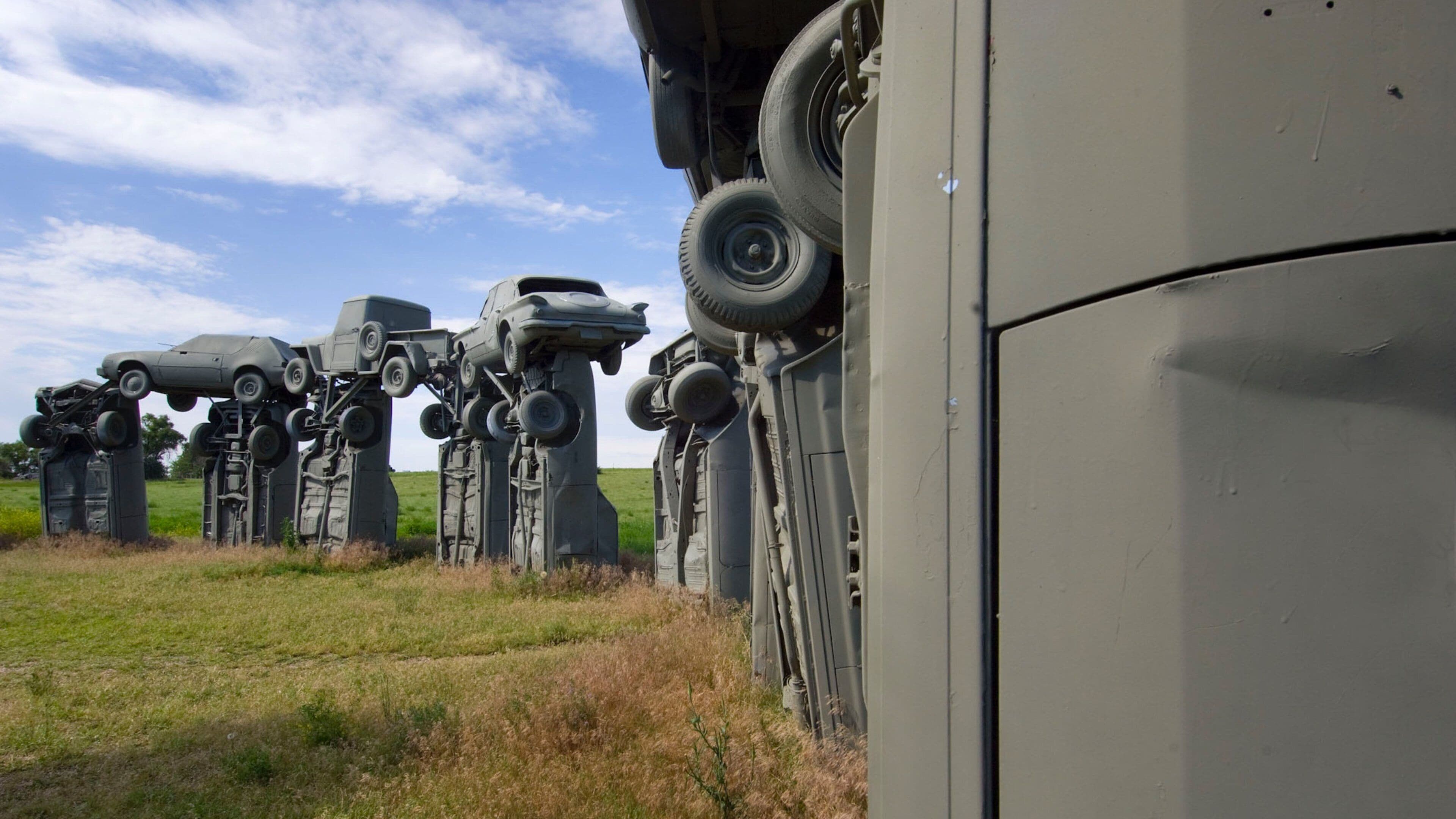 A line of military vehicles with their wheels off the ground, parked in a grassy field.