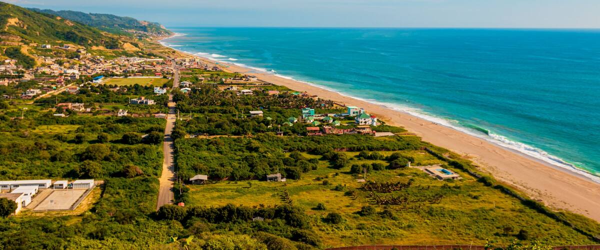 A coastal town with a beach, green hills, and a clear blue sky.