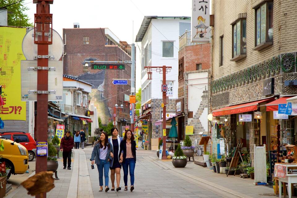 Une rue étroite bordée de boutiques et d’immeubles, dont un restaurant arborant une enseigne coréenne traditionnelle.
