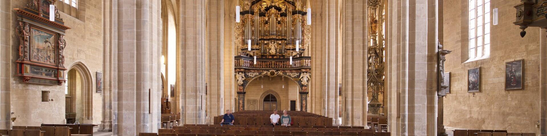A cathedral interior with high vaulted ceilings, large stained glass windows, and ornate religious artwork.