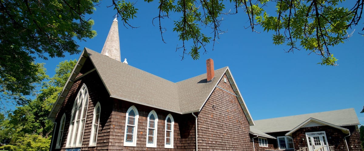 A wooden church with a steeple, surrounded by trees and a clear blue sky.