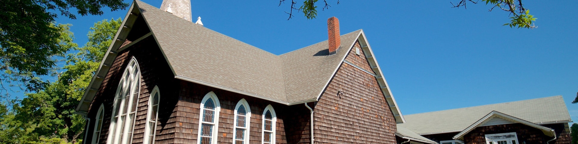 A wooden church with a steeple, surrounded by trees and a clear blue sky.