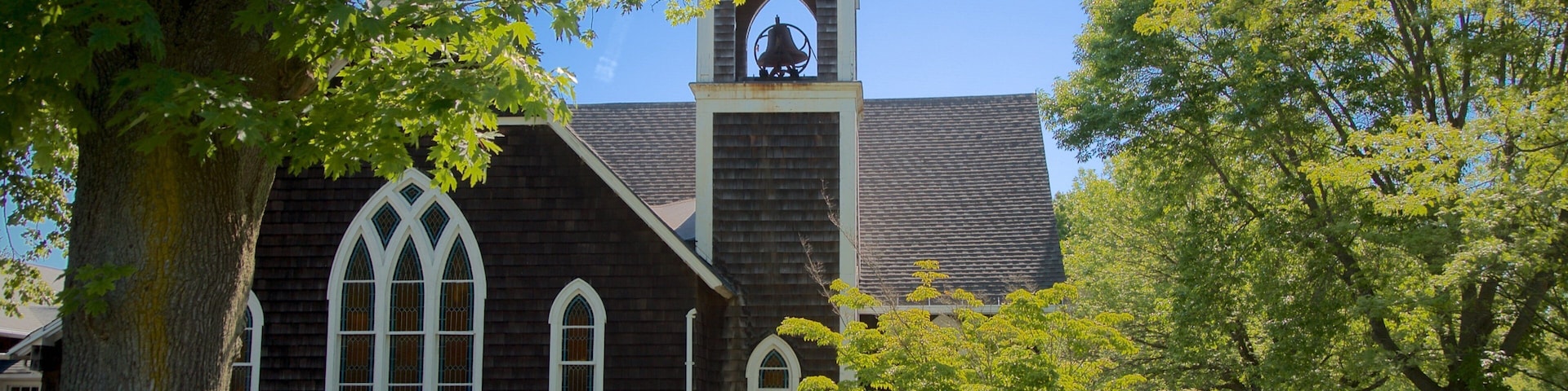 Uma igreja com um campanário, rodeada por árvores e um espaço gramado.