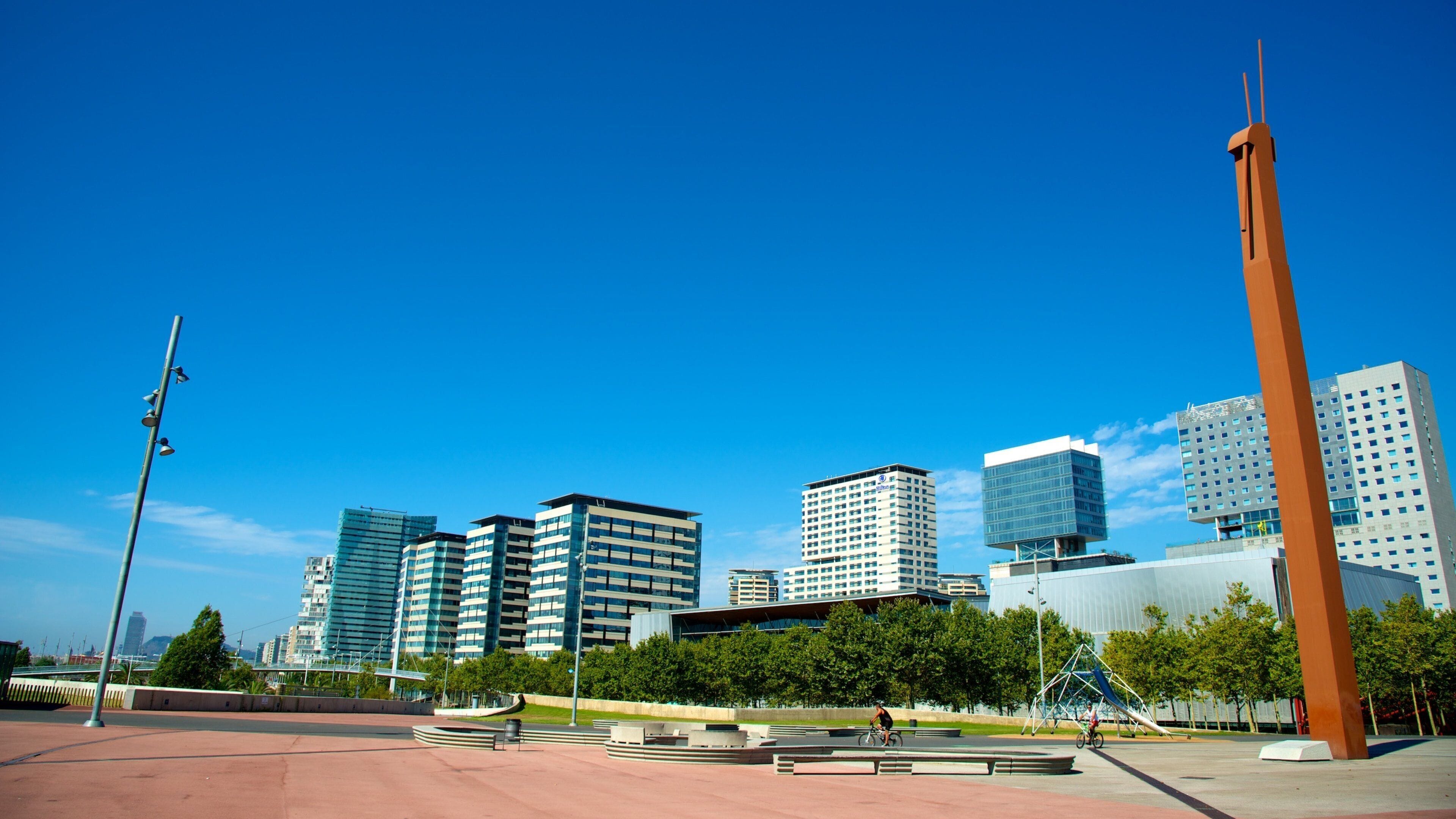 A cityscape with modern high-rise buildings, a prominent orange sculpture, and a clear blue sky.