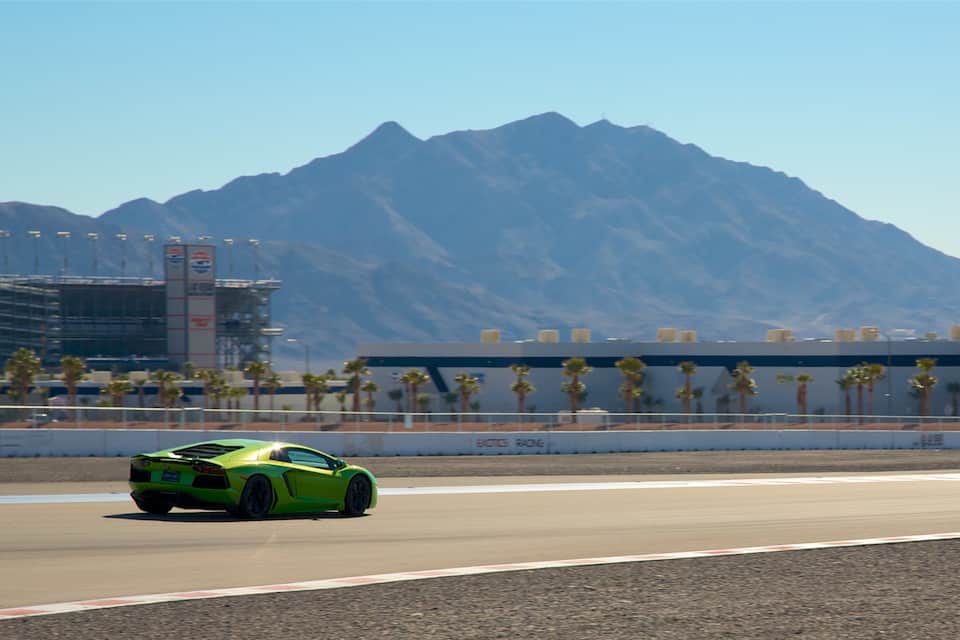 Une voiture de sport verte sur un circuit, avec des montagnes en arrière-plan.