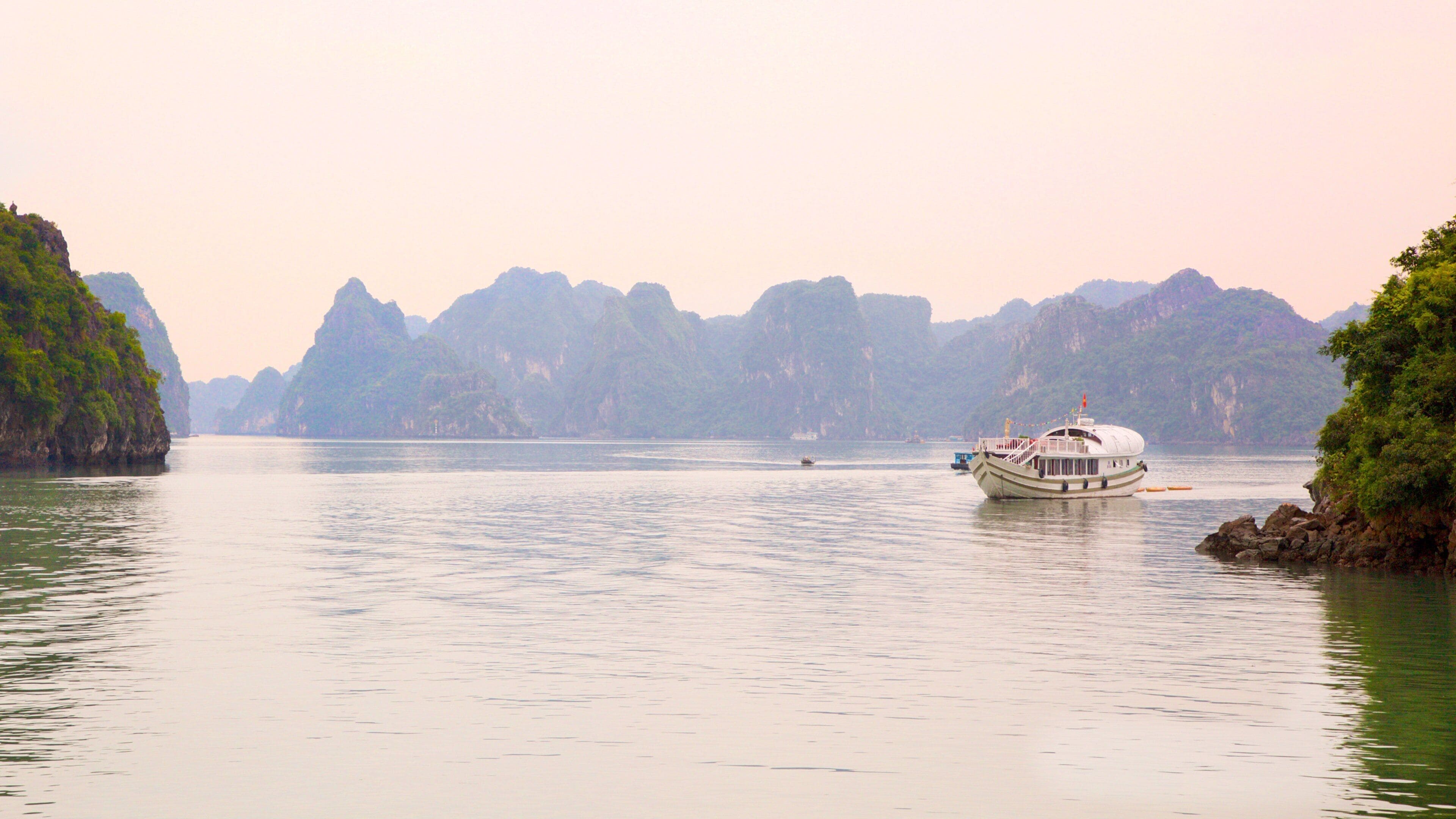 A boat on calm waters surrounded by lush green mountains.