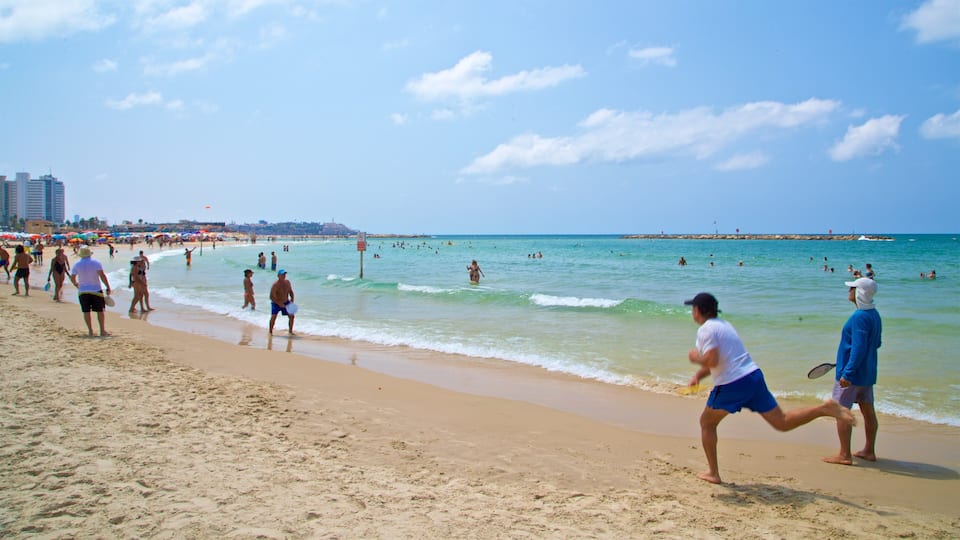 A crowded beach with people playing and swimming in the water.
