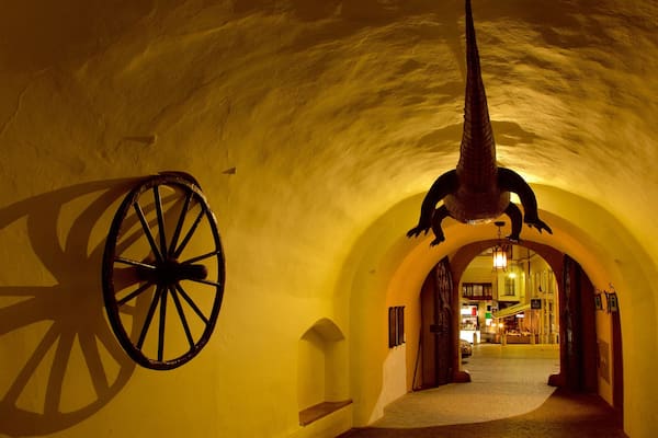 Ein Tunnel mit gelben Wänden, einem großen hölzernen Rad und einer hängenden Skulptur.
