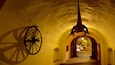 A tunnel with yellow walls, a large wooden wheel, and a hanging sculpture.