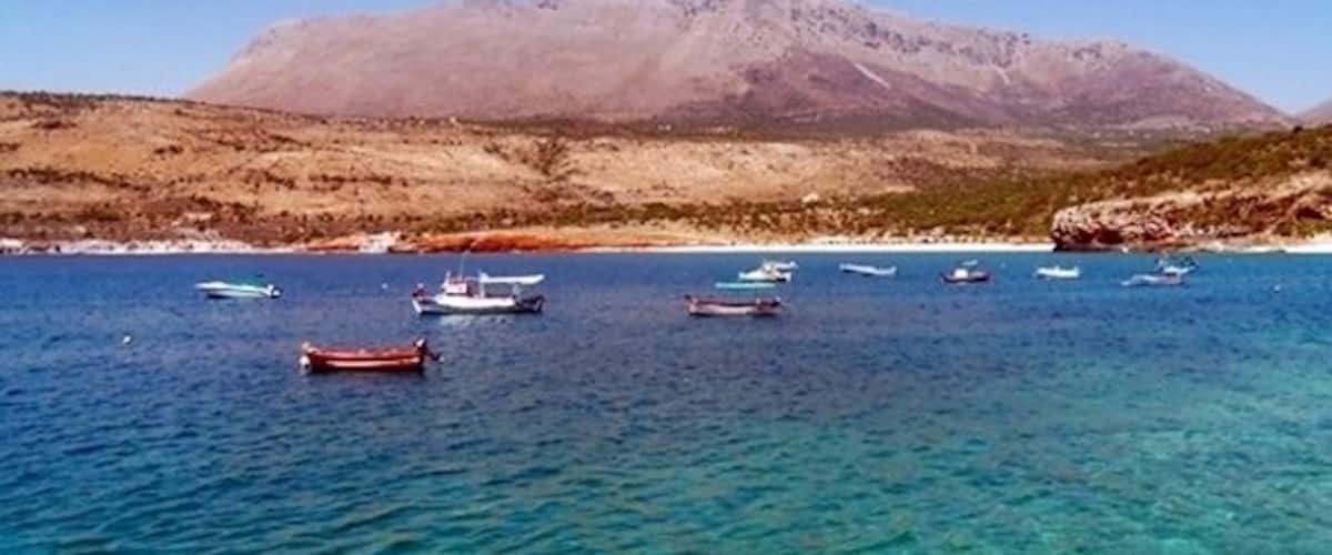 A coastal landscape with boats on clear blue water and a mountain in the background.