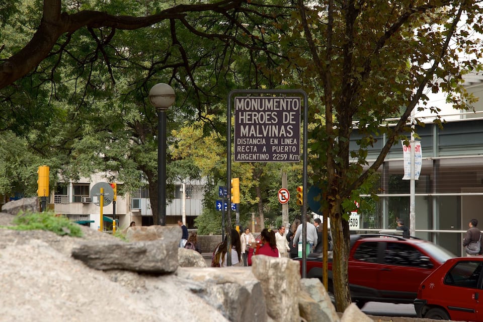 A monument sign, a red car, and a building in the background.