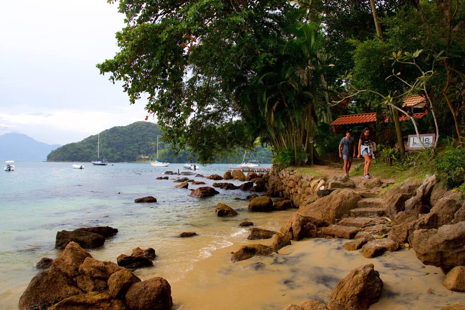 Uma costa rochosa com barcos na água, uma montanha ao fundo e um restaurante chamado "L'le".