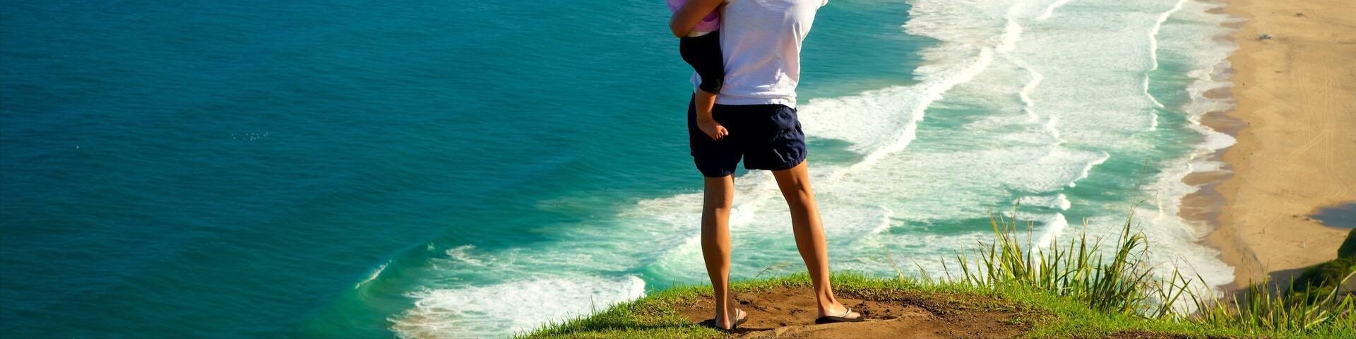 Una mujer y un niño observan un paisaje costero con playa y acantilados.