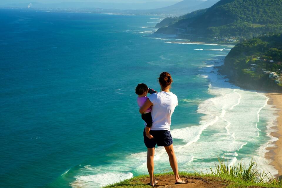 Eine Frau und ein Kind blicken auf eine Küstenlandschaft mit Strand und Klippen.