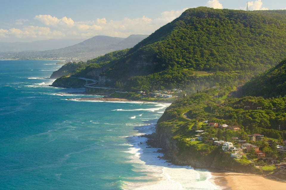Un paysage côtier avec une route sinueuse qui longe les falaises, une plage et, en arrière-plan, des montagnes.