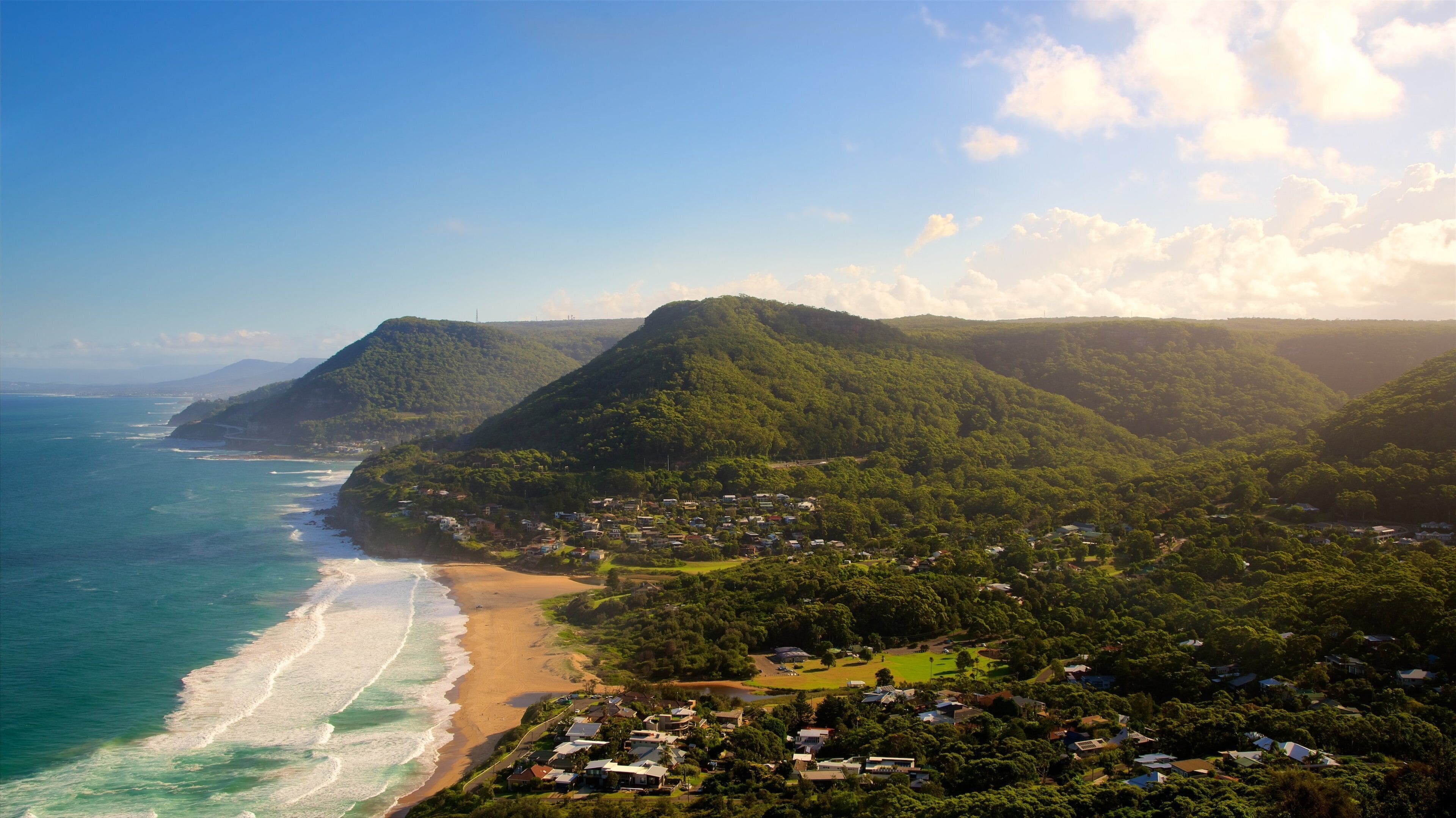 A coastal town with a beach, houses, and lush green hills.