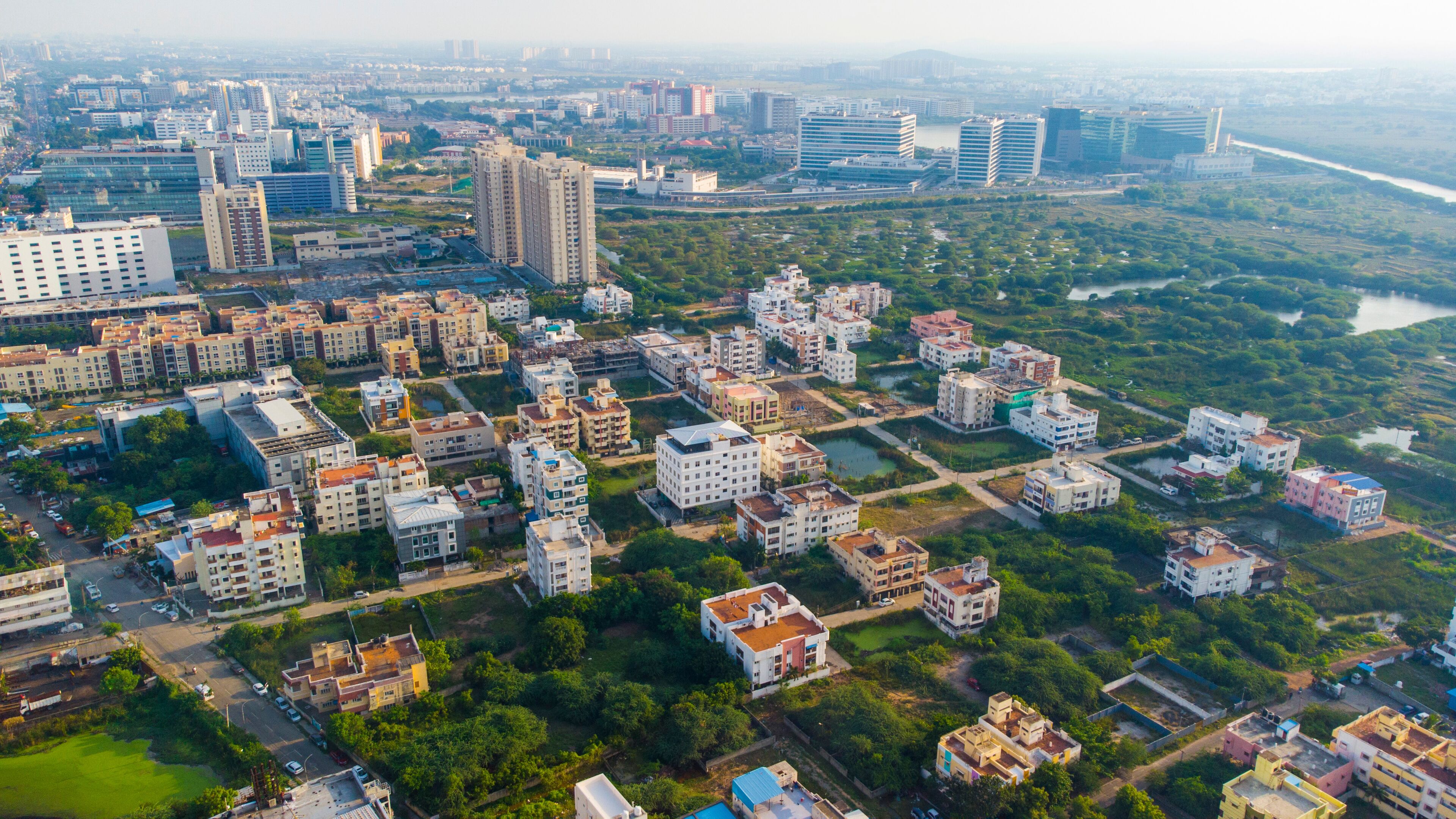 An aerial view of a city with dense residential buildings, a river, and distant high-rise buildings.