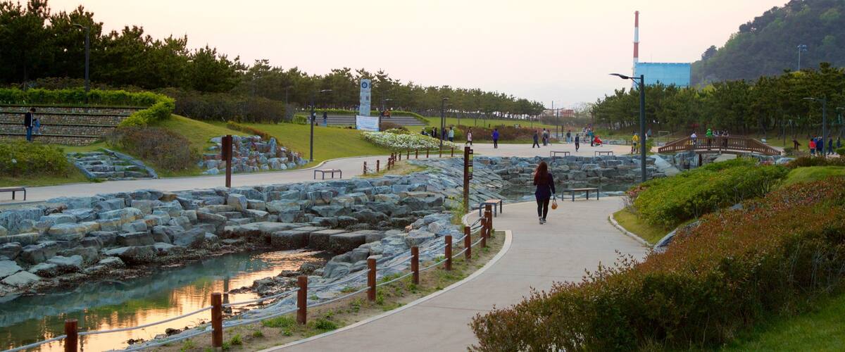 A riverside park with a walking path, rocks, and greenery.