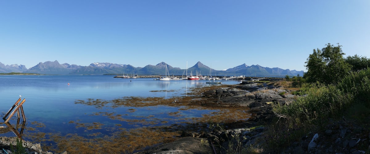 A calm fjord with boats, rocky shores, and mountains in the background.
