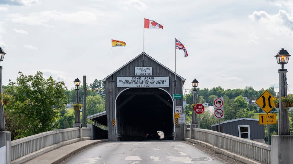 A covered bridge with flags, signs indicating height and lane restrictions, and a sign stating it's the longest covered bridge in the world.