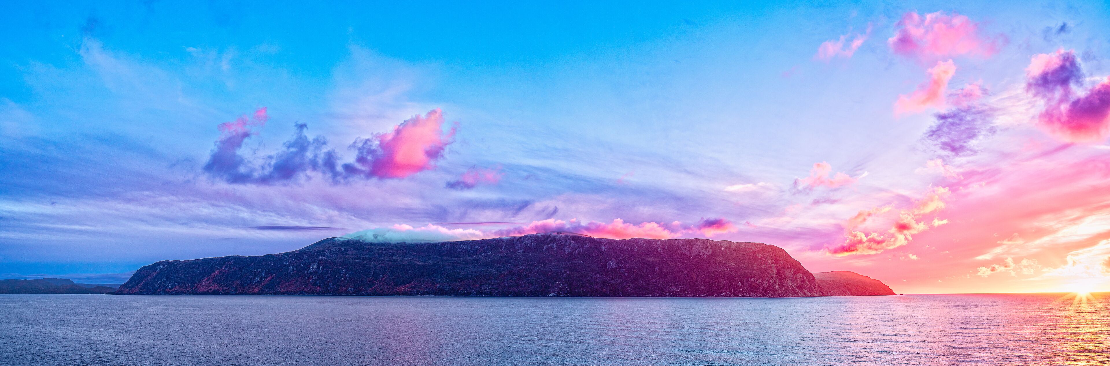 A mountainous landscape with a sunset over a calm sea.