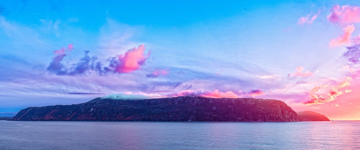 A mountainous landscape with a sunset over a calm sea.