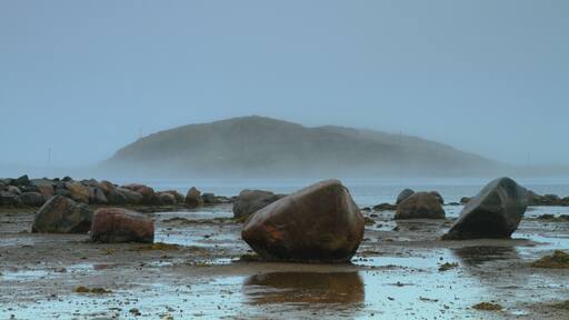 A rocky beach with large boulders and a misty mountain in the background.