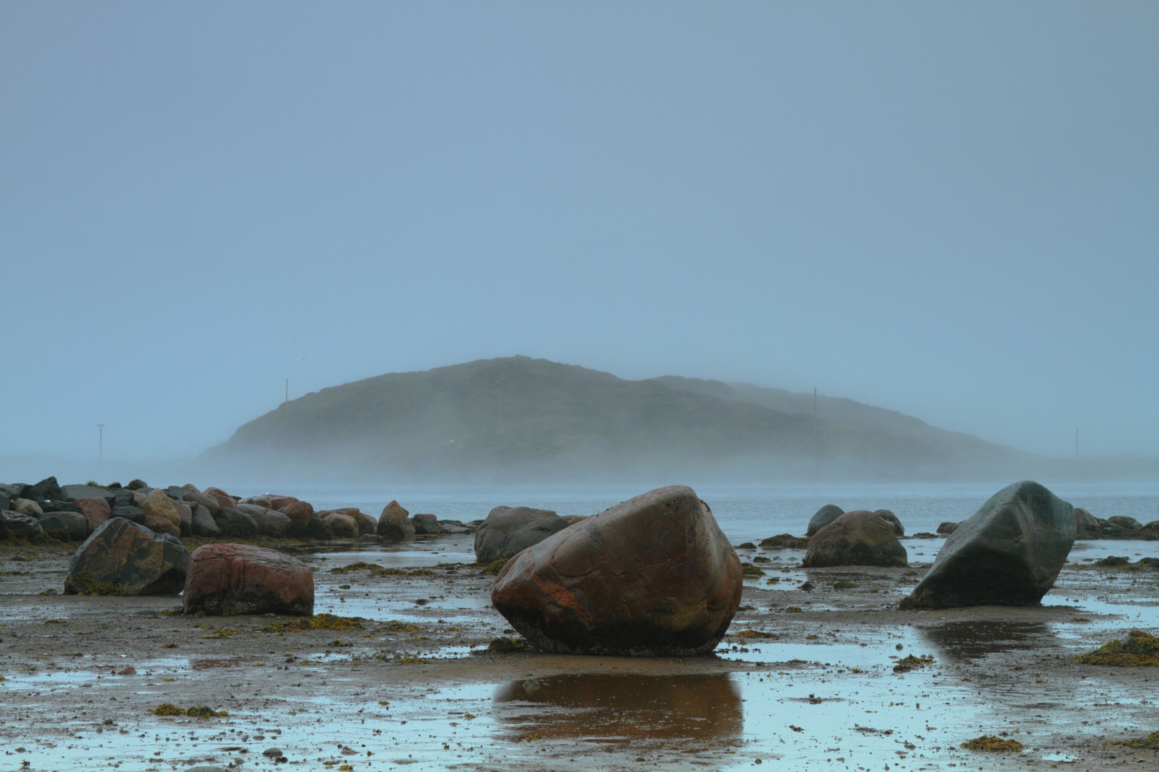 A rocky beach with large boulders and a misty mountain in the background.