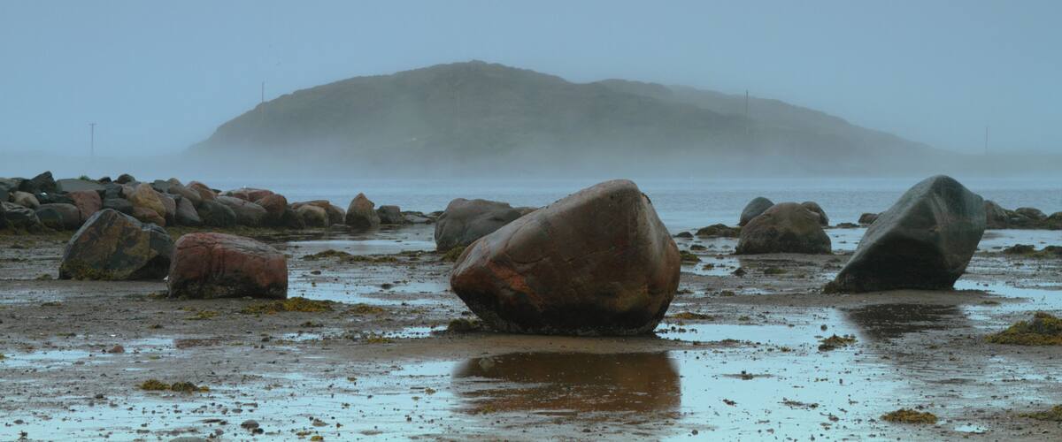 A rocky beach with large boulders and a misty mountain in the background.