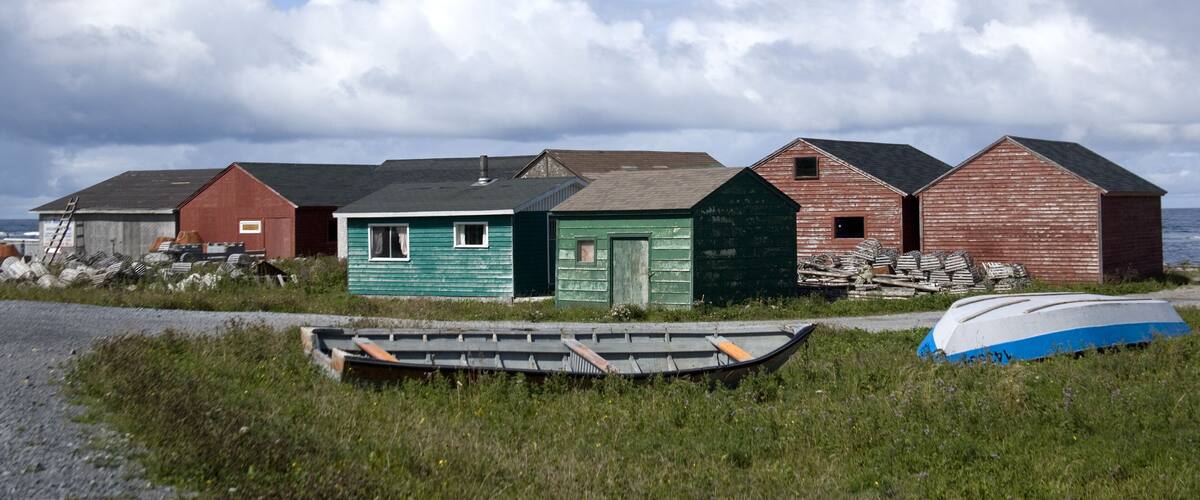 A row of wooden buildings by the sea, a small boat, and a gravel path.